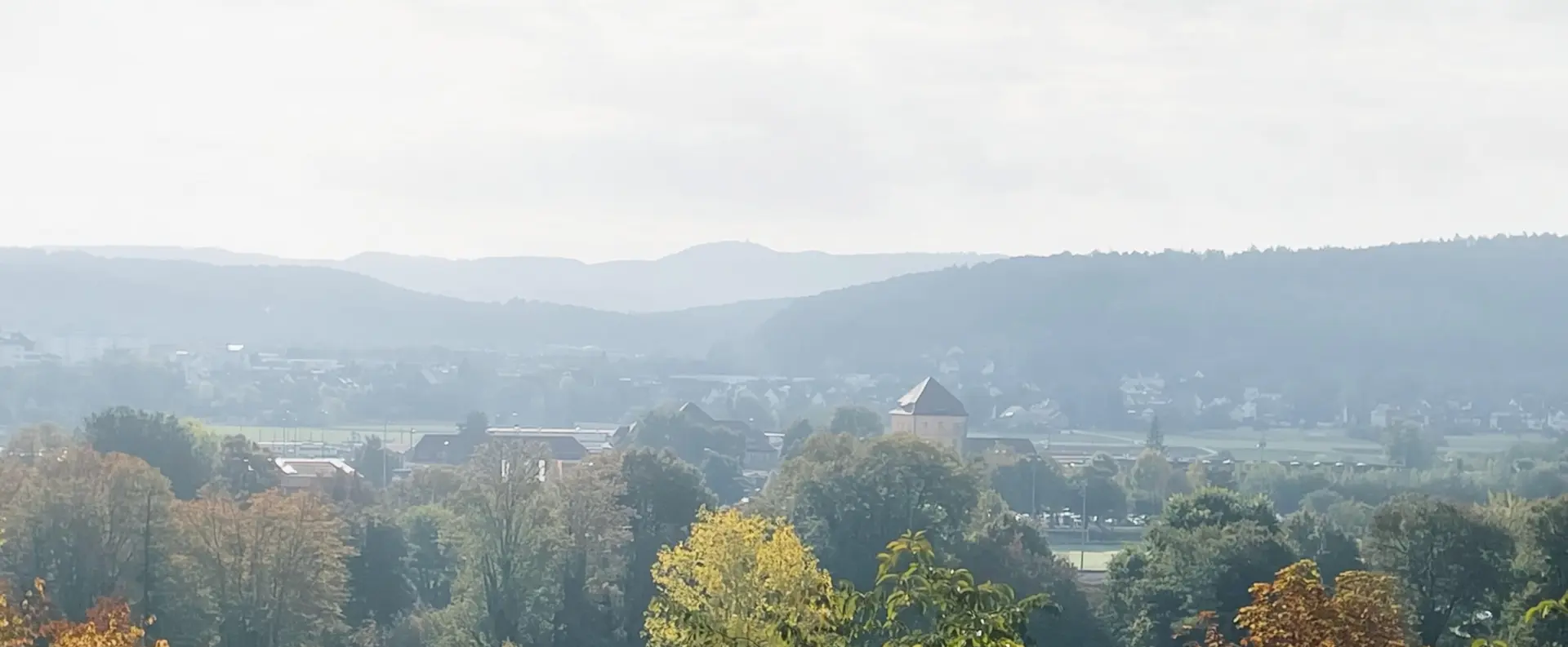 Neblige Hügellandschaft mit Dorf, Kirche und herbstlichen Bäumen